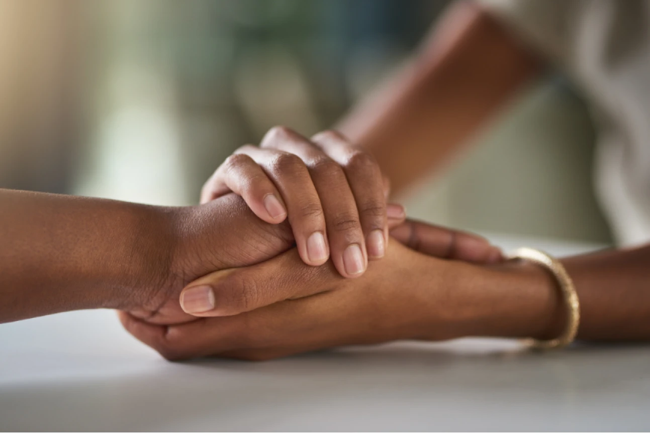 Two people holding hands in a gesture of support and comfort, one wearing a gold bracelet.