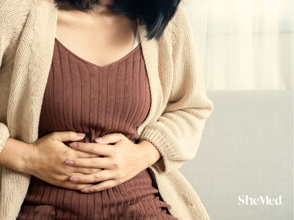 Woman sitting on a sofa holding her stomach, depicting abdominal discomfort or pain.