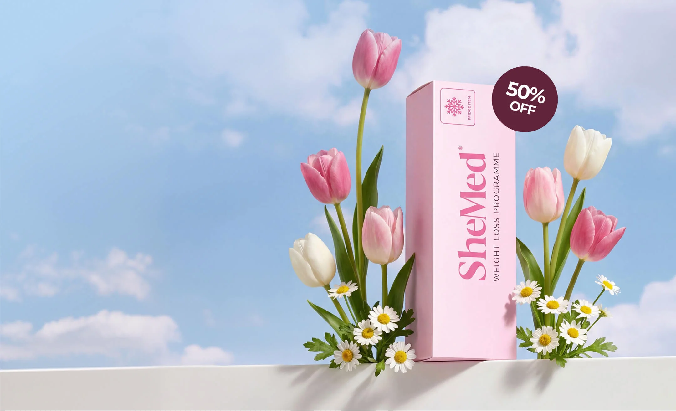 Pink SheMed weight loss programme box surrounded by pink and white tulips and daisies with 50% off tag against a blue sky background.