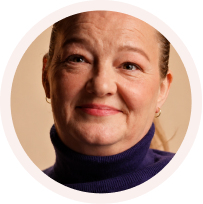 Close-up portrait of a smiling middle-aged woman wearing a dark turtleneck and small hoop earrings.