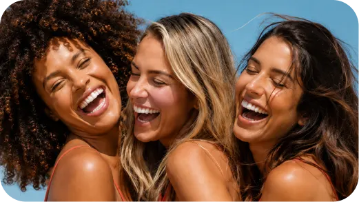 Three diverse women with braces laughing closely together against a blue background.