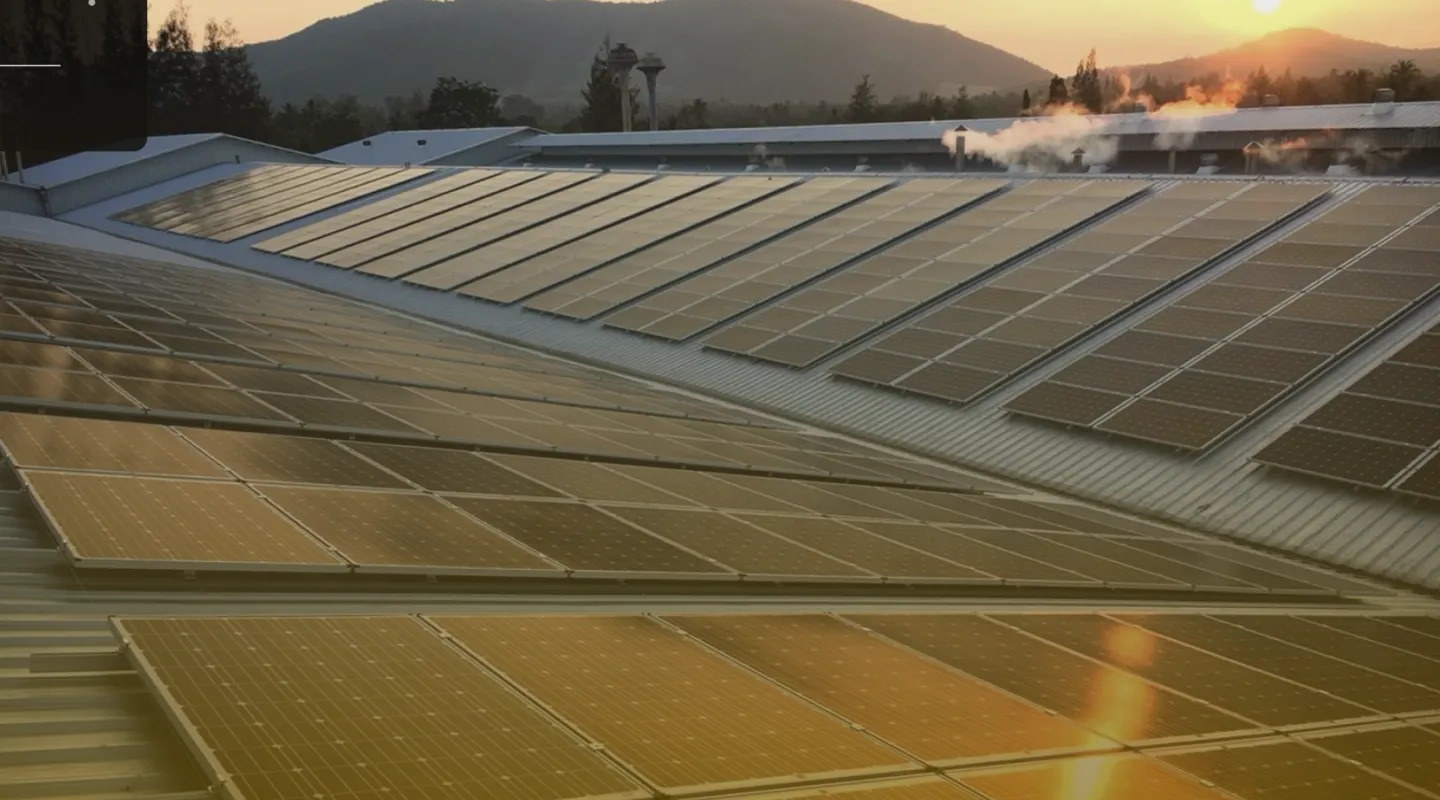 Rows of solar panels installed on a rooftop at sunset with mountains in the background and steam rising from buildings.
