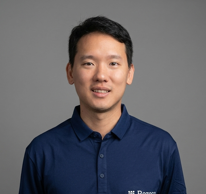 Man wearing a navy blue polo shirt with the logo 'Rezeca' on the left chest, standing against a gray background.