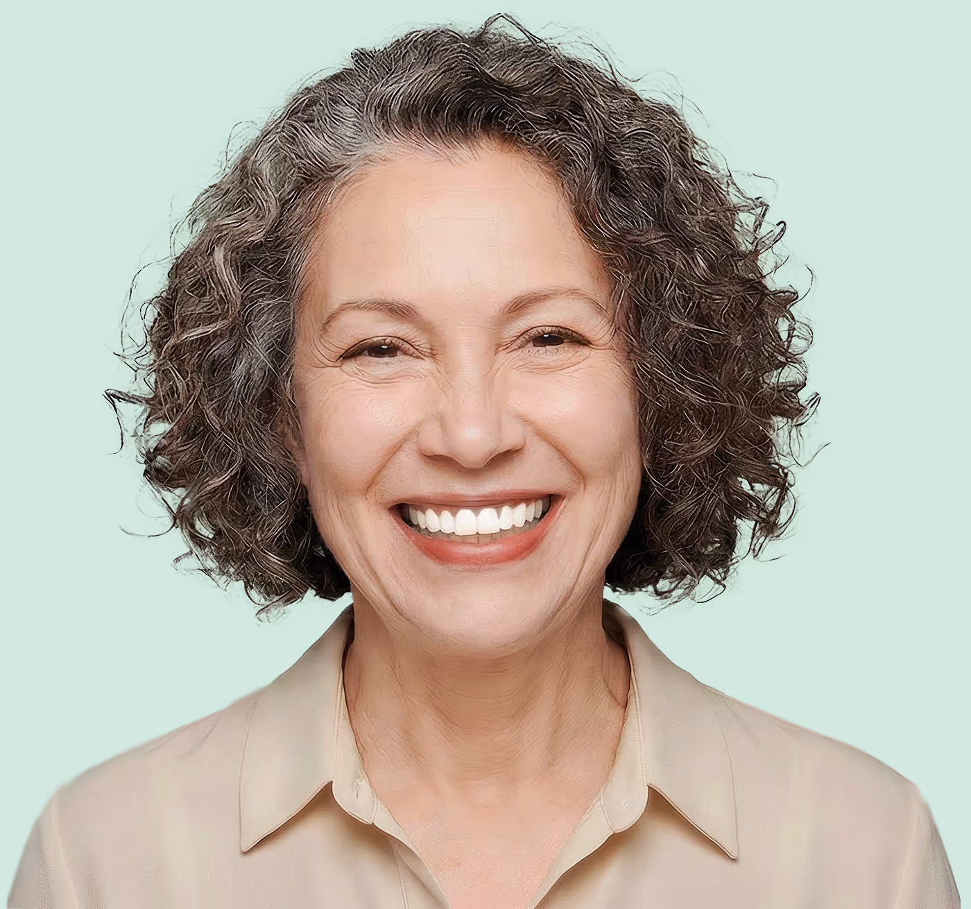 Smiling middle-aged woman with curly salt-and-pepper hair against a light mint background.