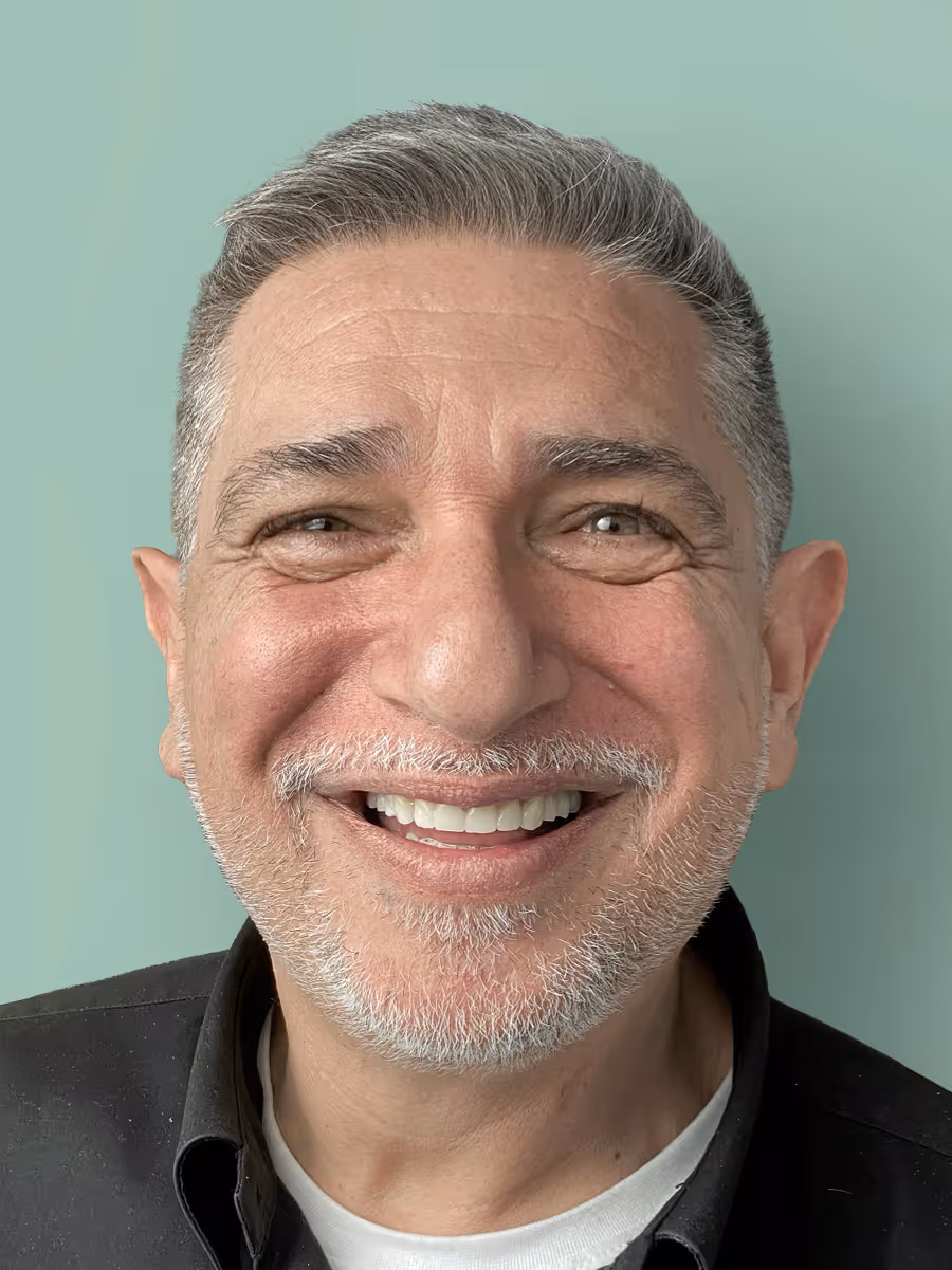 Close-up of a smiling middle-aged man with salt-and-pepper hair and beard against a light green background.