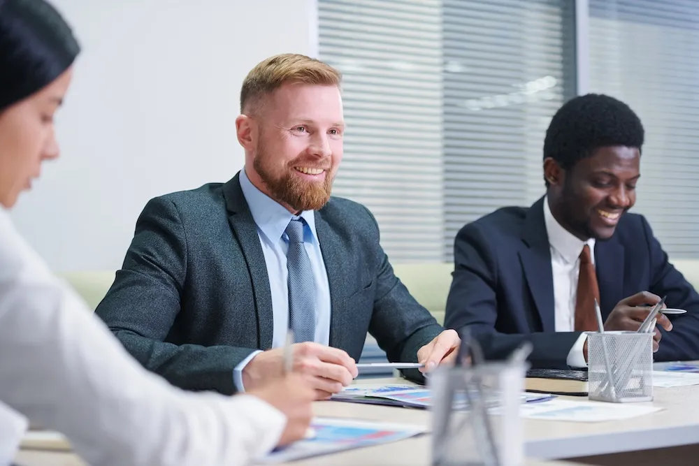 Three business professionals in suits engaged in a meeting discussing documents at a conference table.