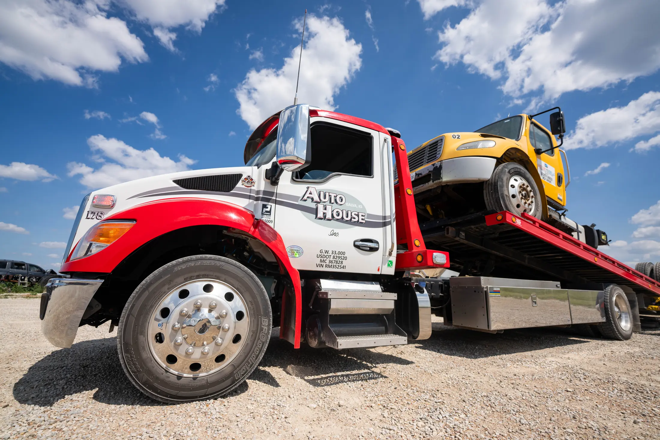 Auto House rollback tow truck loading a yellow box truck