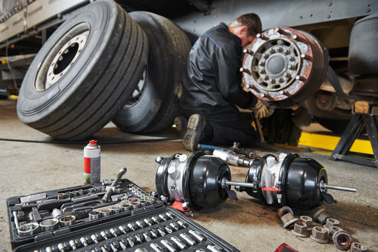 Mechanic servicing brake drums and air brake chambers under a trailer