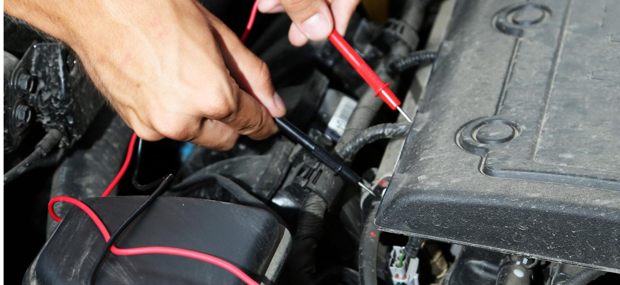 Hands testing a car engine with multimeter probes