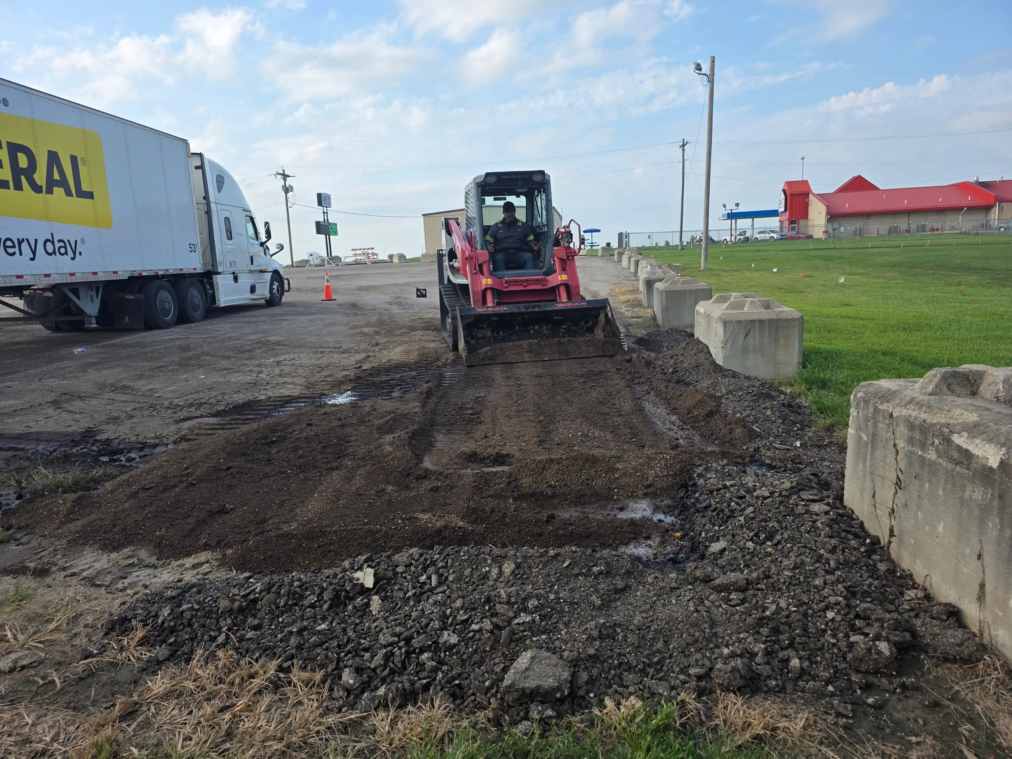 Auto House track loader scraping spilled material off pavement beside a semi