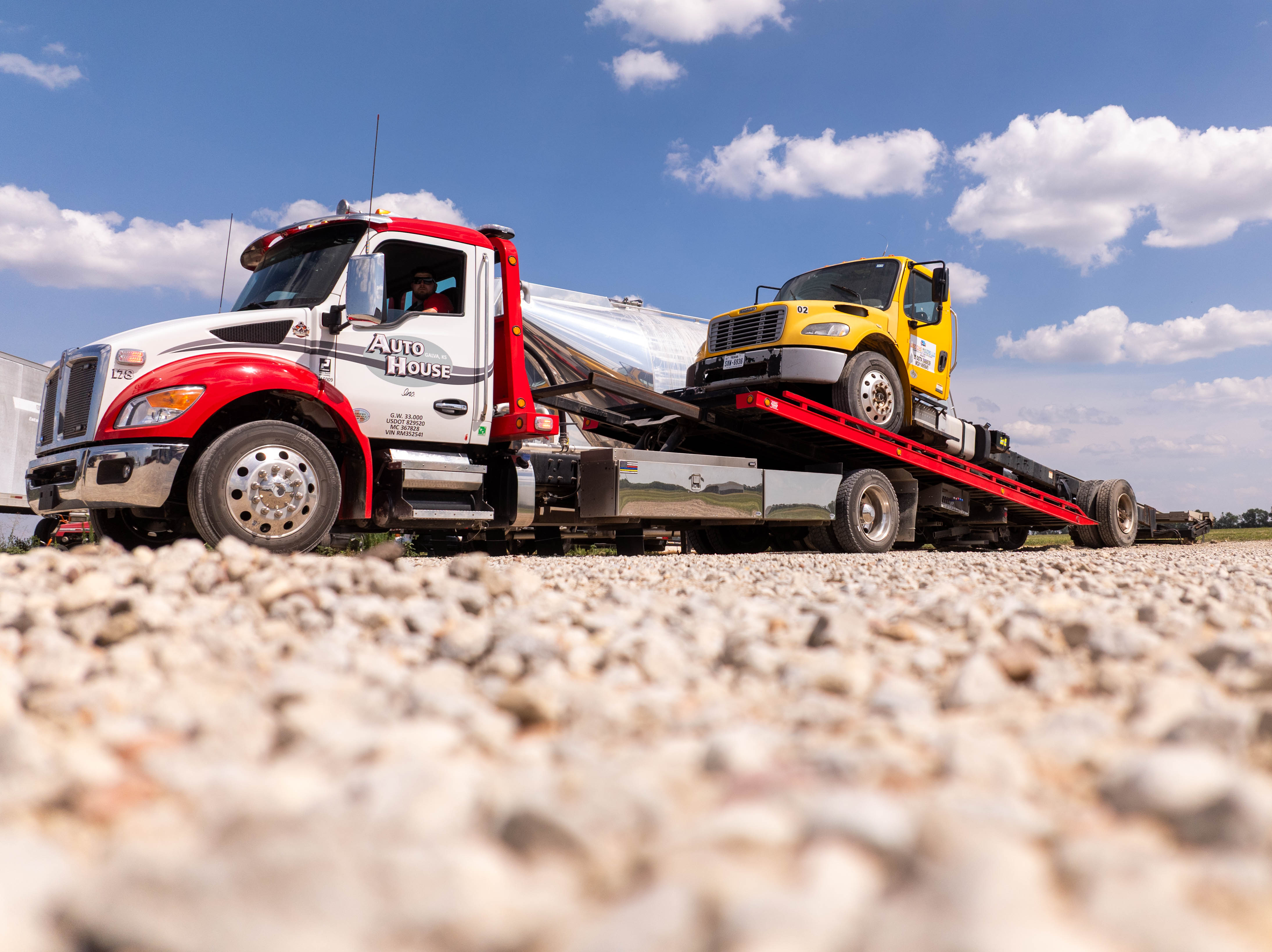 Auto House rollback carrying a yellow box truck on a gravel road