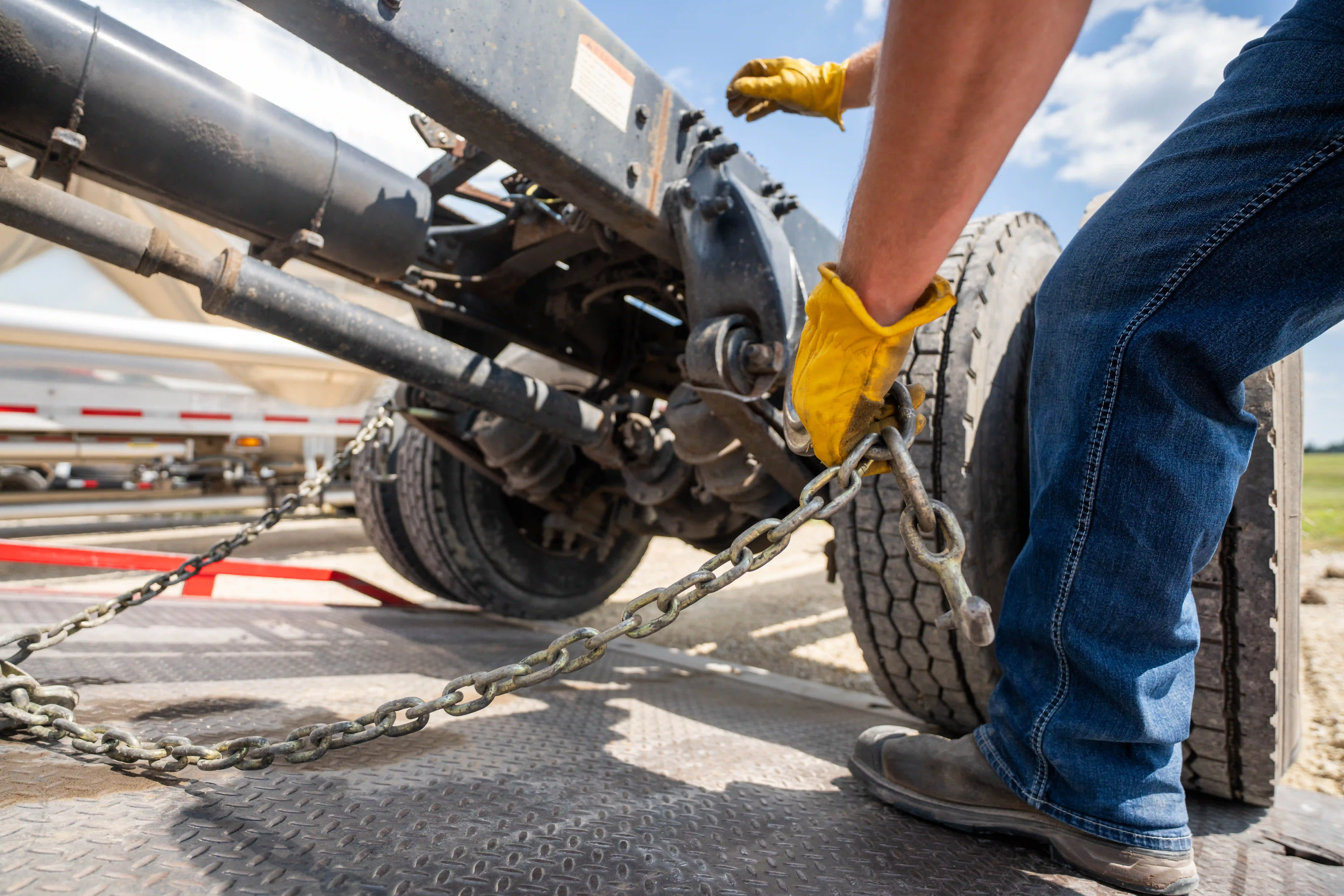Technician chaining down a tanker trailer axle on a rollback deck