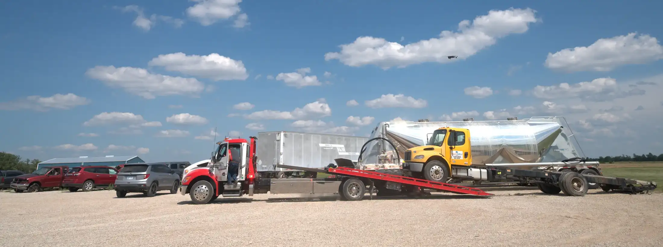 Auto House rollback loading a yellow truck beside stainless tank trailers