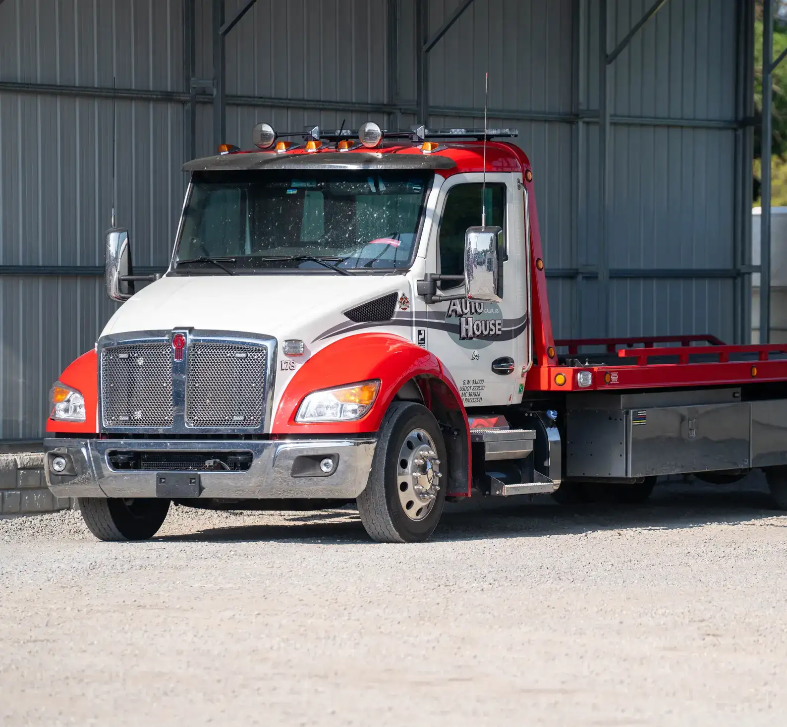 Red and white Auto House rollback tow truck parked at the shop