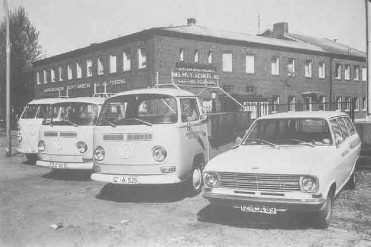 Altes Foto mit VW-Firmenbuschen, im Hintergrund ist das Firmengebäude zu sehen