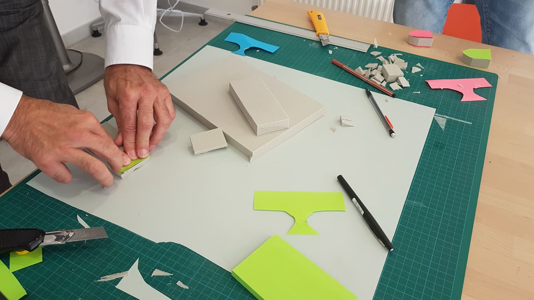 Person cutting and assembling colored foam or craft sheets on a green cutting mat and white work surface.