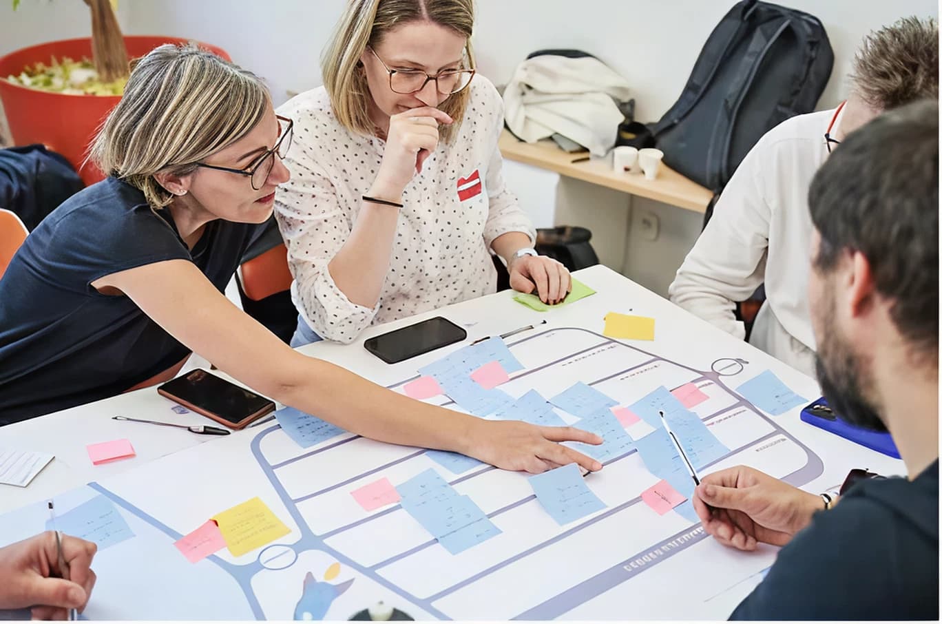 Quatre adultes discutant autour d'une table avec des notes autocollantes colorées sur un diagramme posé devant eux.