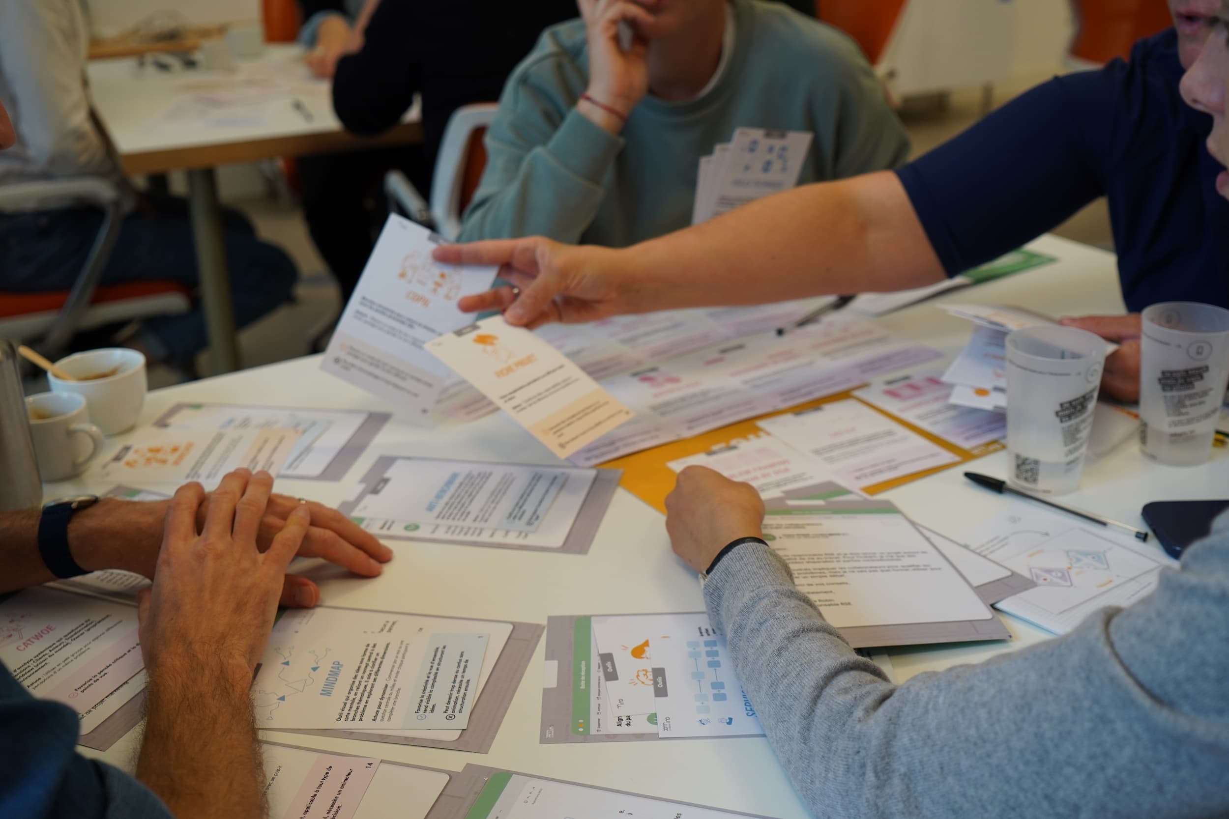 Personne tendant des cartes d'information pendant une discussion de groupe autour d'une table avec plusieurs documents et tasses.