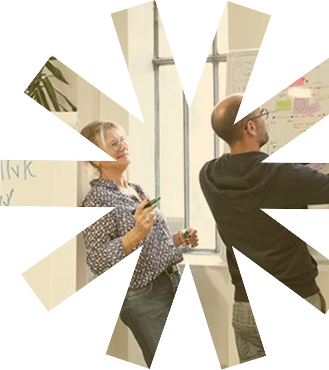 Deux collègues discutant et planifiant devant un tableau blanc avec des notes autocollantes dans un bureau lumineux.