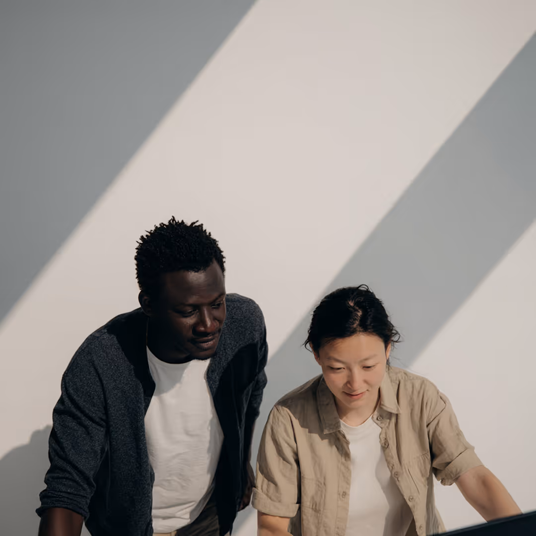 Två personer samarbetar och tittar på en datorskärm i ett solbelyst rum.