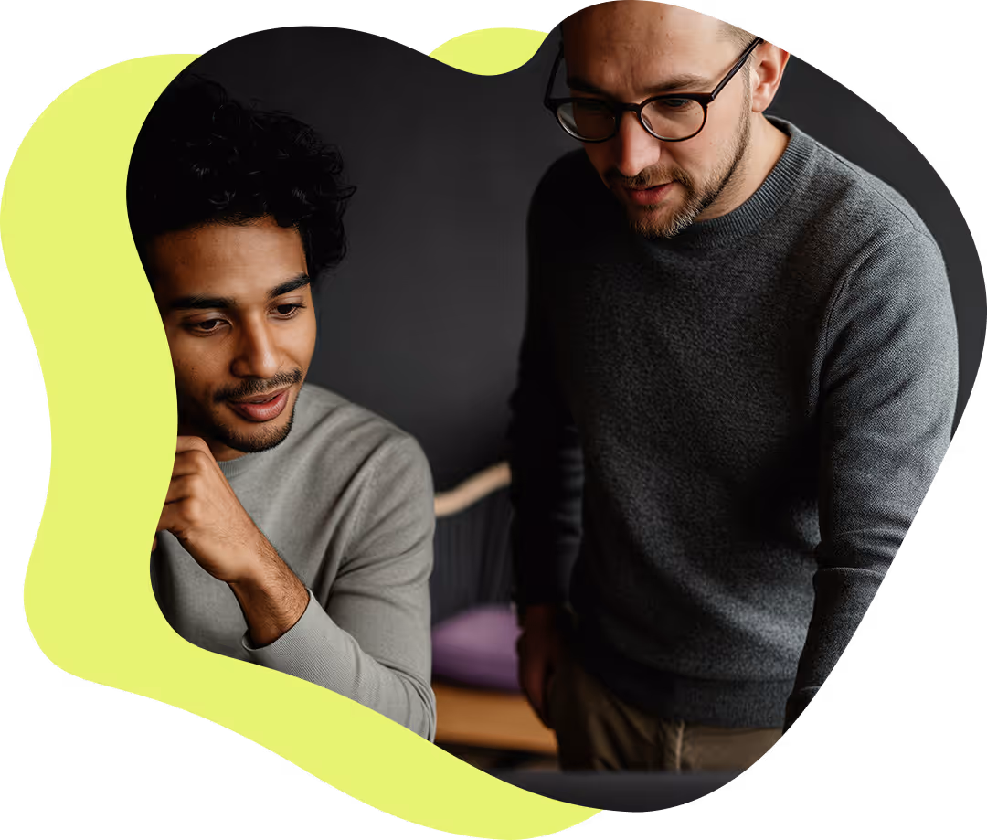 Två män i tröjor som diskuterar något medan de tittar på en bärbar dator.