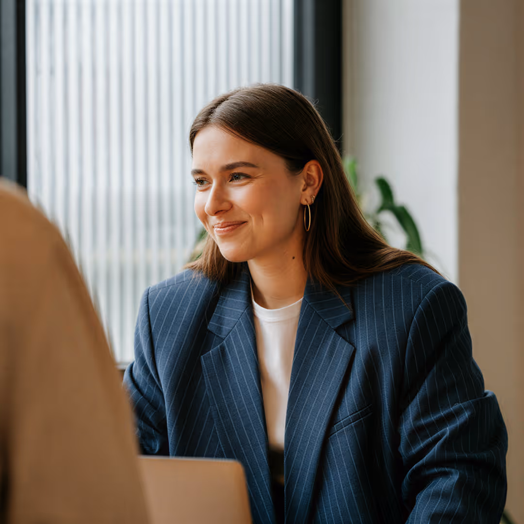 Leende kvinna i blå kavaj och vita t-shirt i ett professionellt samtal.