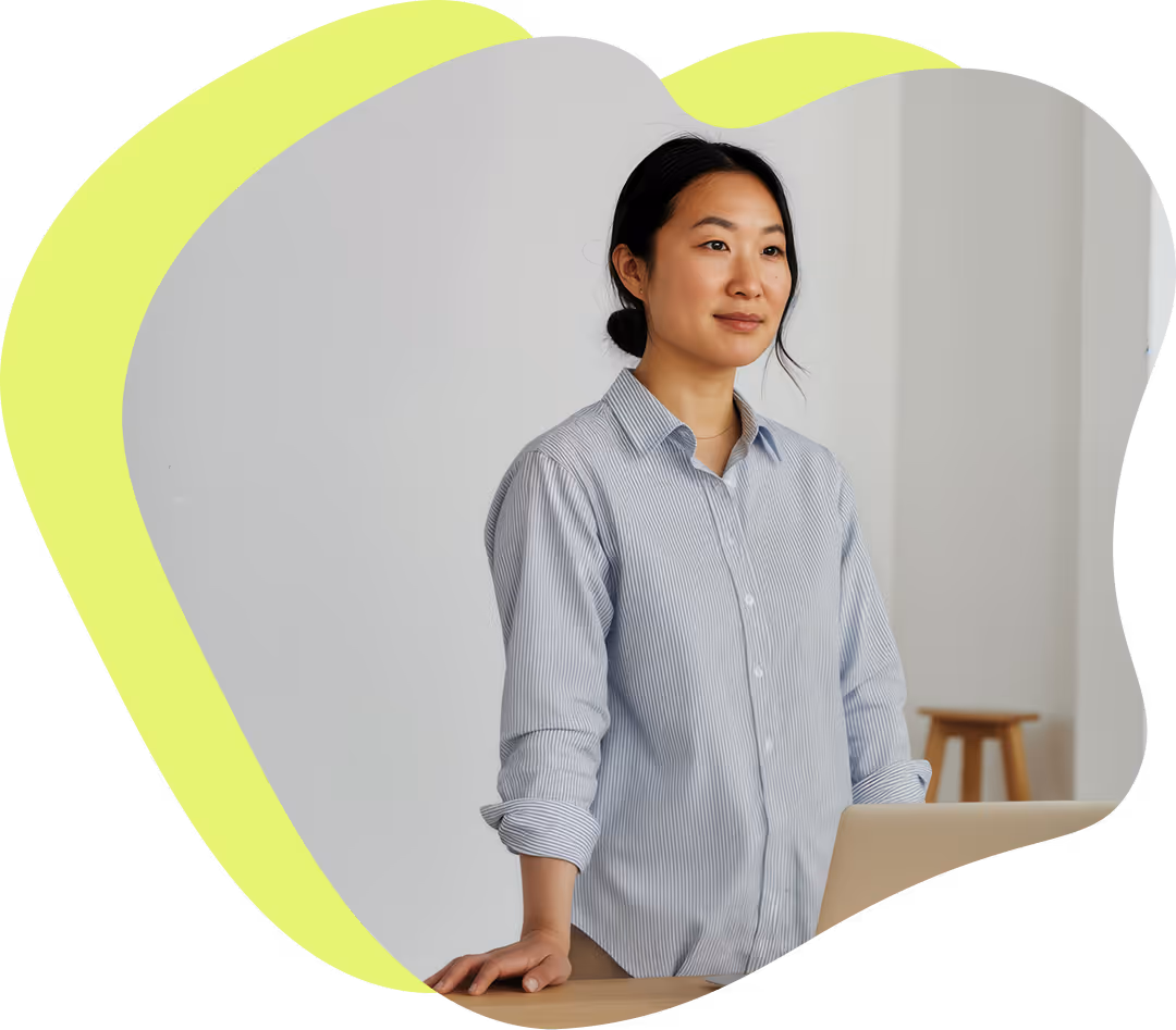 Kvinna i randig skjorta står vid ett bord med en bärbar dator och tittar framåt med ett lugnt uttryck.