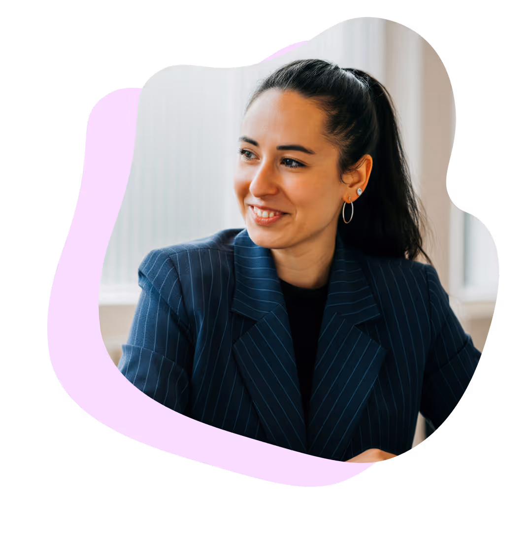 Kvinna med svart hästsvans och blå randig kavaj ler medan hon tittar åt sidan.