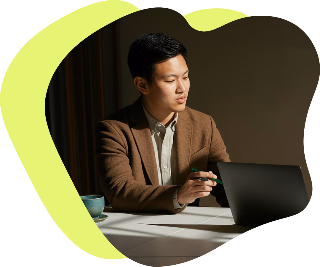 Man i brunt kavaj sitter vid ett bord och pekar på en bärbar dator med en penna.