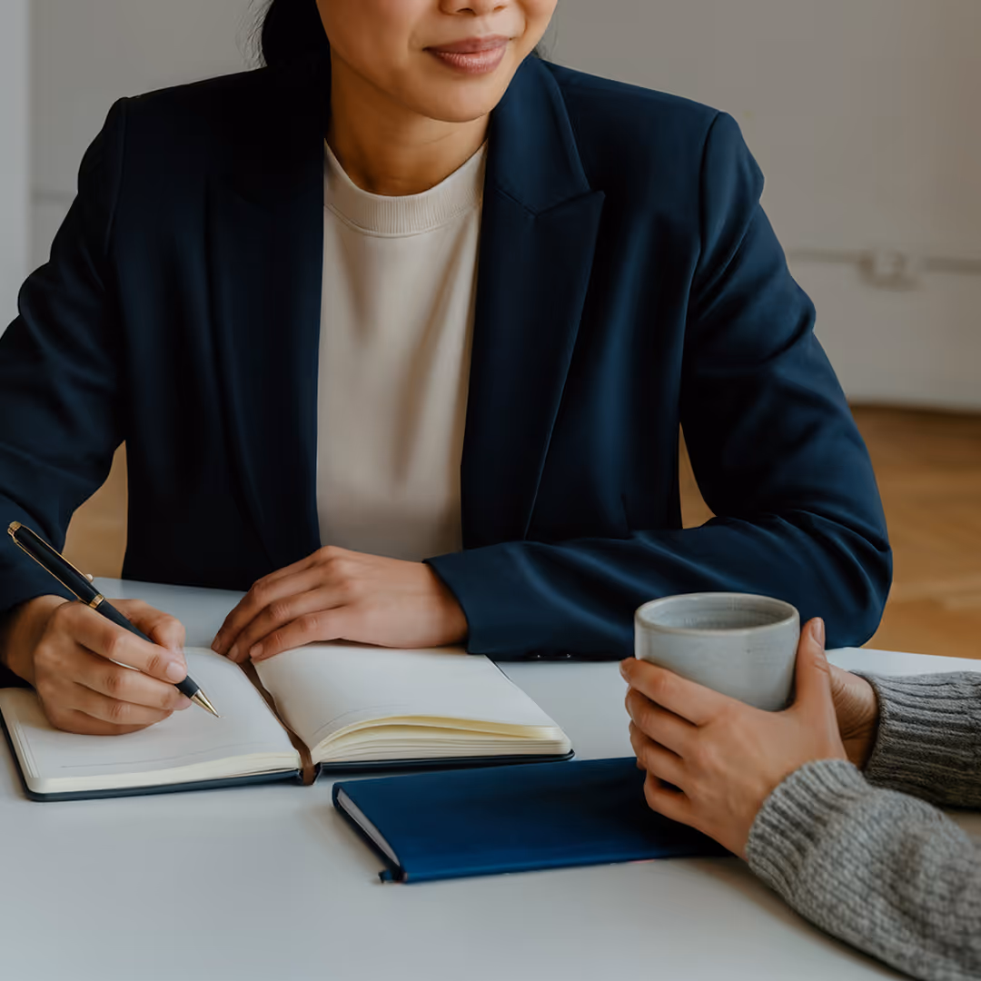 Två personer i samtal, en skriver i en öppen anteckningsbok medan den andra håller en kopp.