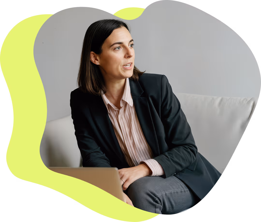 Kvinna i svart kavaj och randig skjorta sitter på en soffa och talar, med en laptop framför sig.