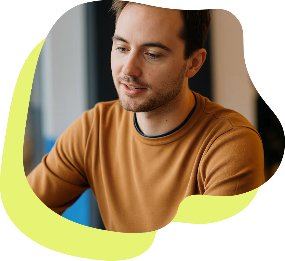 En ung man med brunt hår och skägg, klädd i en brun tröja, ser koncentrerat neråt.