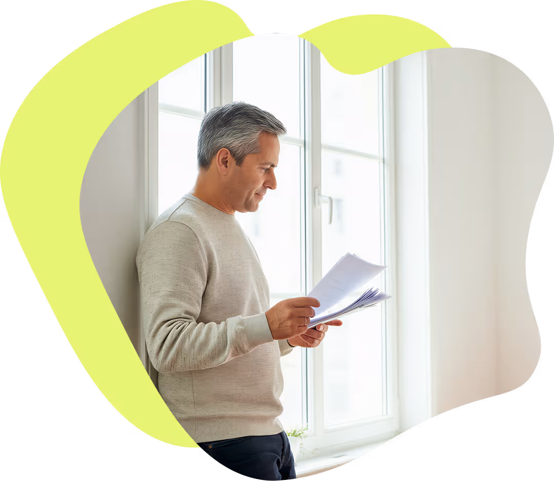 Man i beige tröja läser dokument vid ett stort fönster.