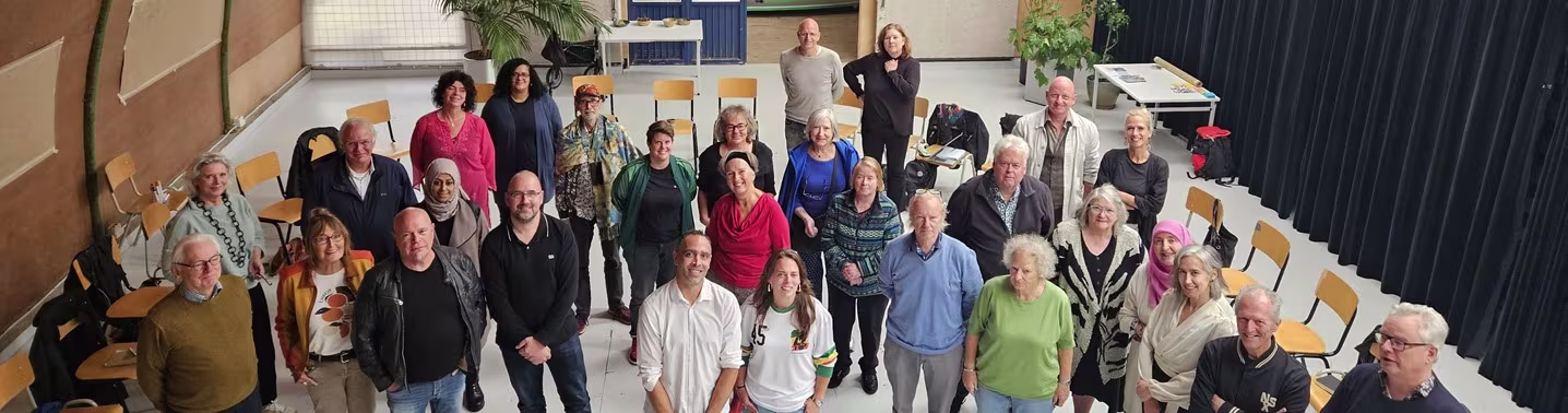 Groepsfoto van ongeveer 30 medewerkers en bewoners die samen poseren in een grote ruimte met stoelen.
