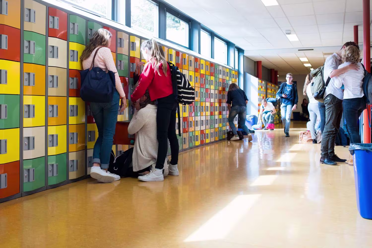 Leerlingen bij kleurrijke kluisjes in een schoolgang, sommigen pakken spullen uit hun kluisjes.