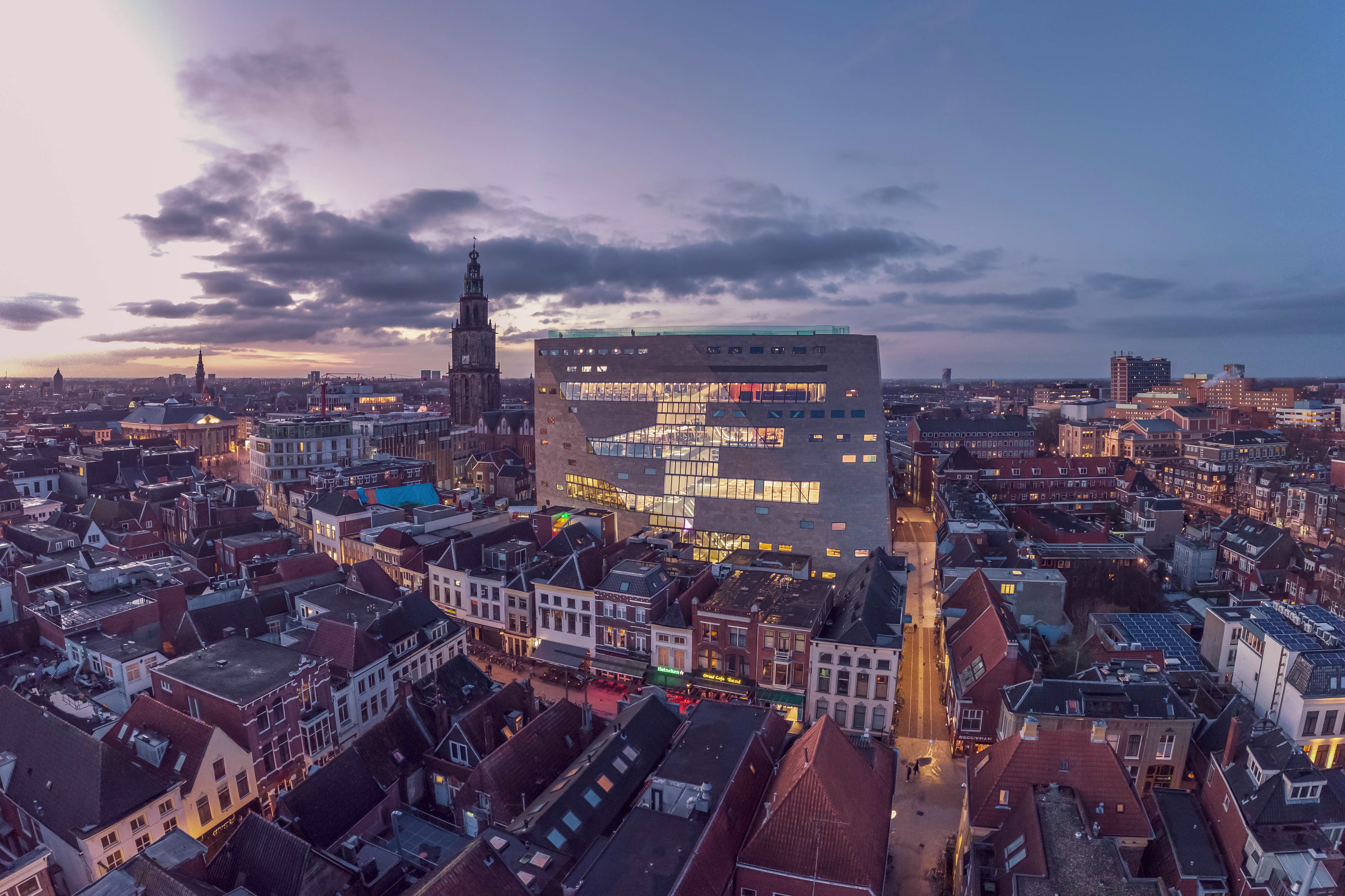 Luchtfoto van Groningen bij zonsondergang met het moderne Forum gebouw prominent in het centrum tussen historische panden.