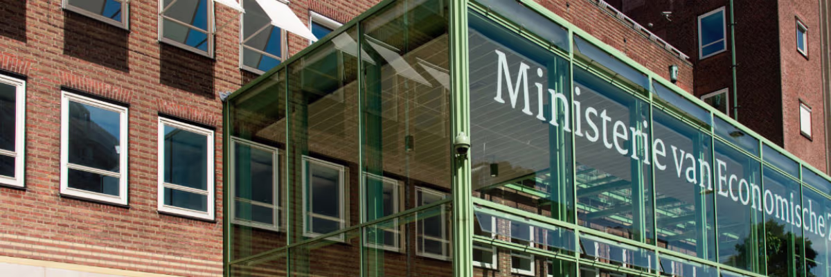 Glazen pui van het Ministerie van Economische Zaken en Klimaat met moderne architectuur en bakstenen gebouw op achtergrond.