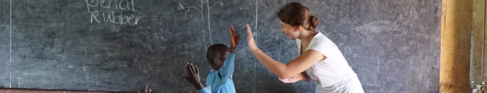 Een lerares en leerling geven elkaar een high five in een klaslokaal met schoolbord op de achtergrond.