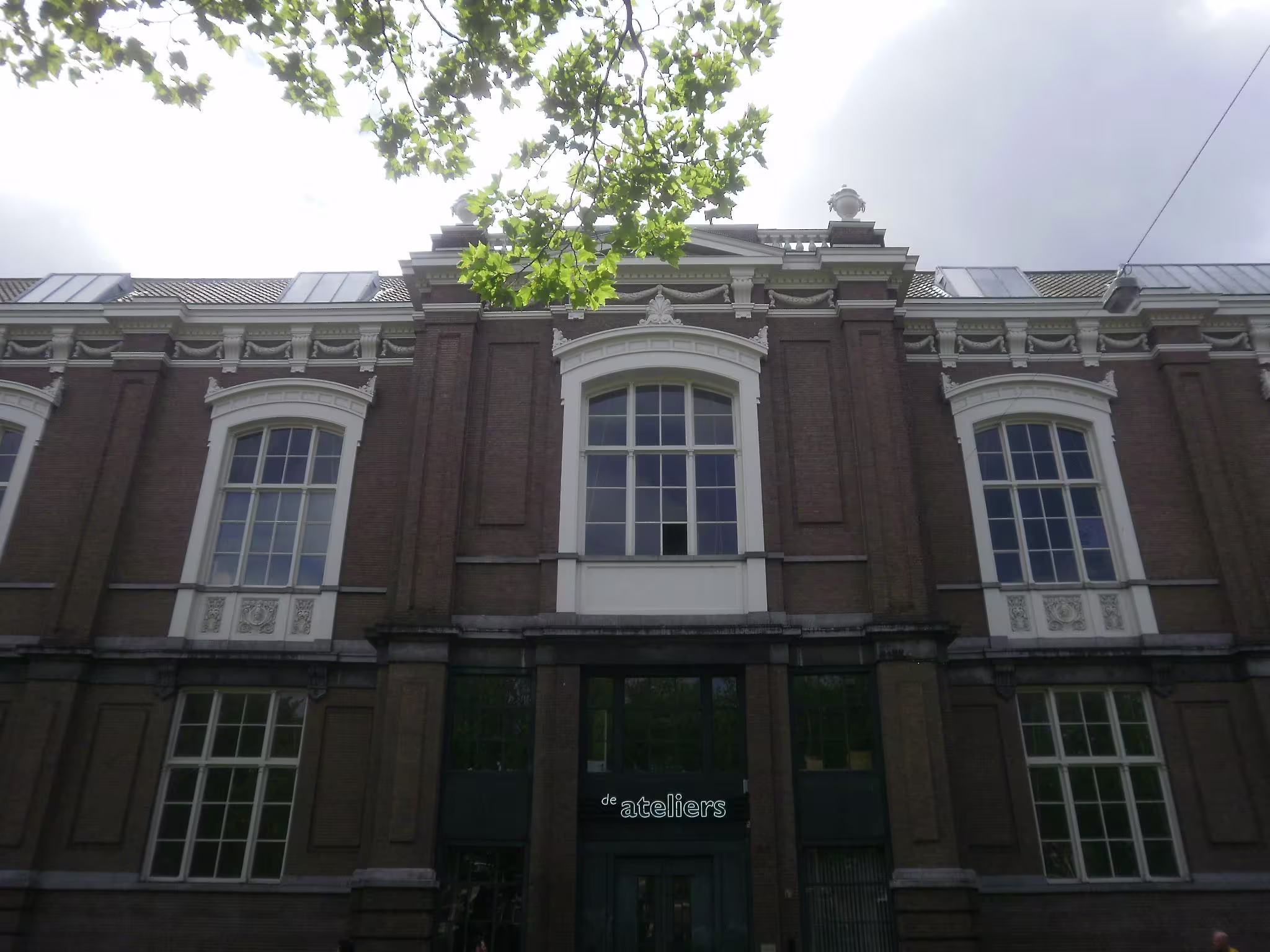 Historisch bakstenen gebouw met witte details en grote ramen, met "de ateliers" boven de groene toegangsdeur.