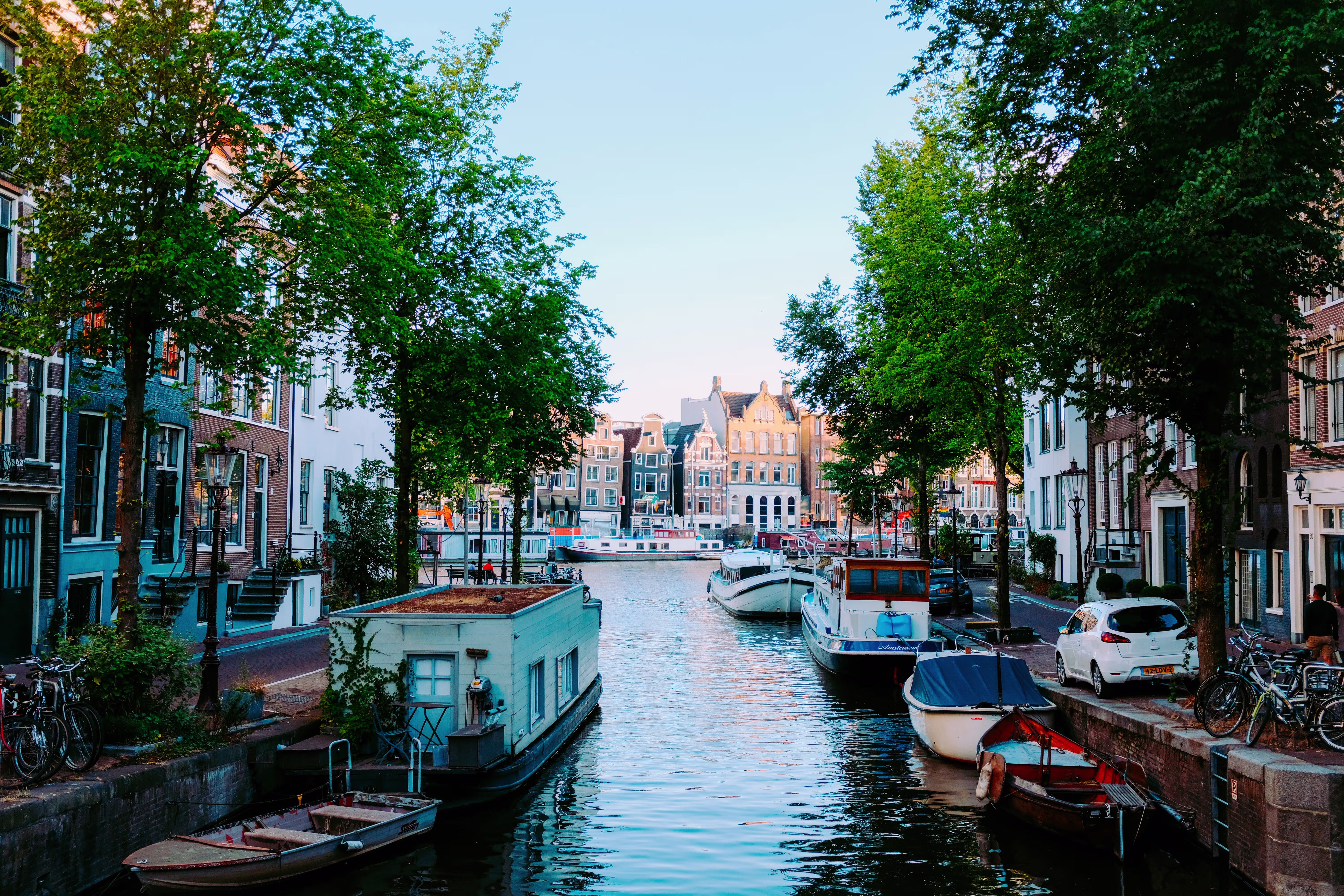 Een pittoreske Amsterdamse gracht met historische huizen, boten en groene bomen langs het water.