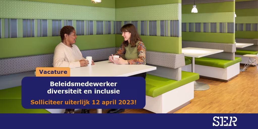 Twee vrouwen voeren een gesprek aan een tafel in een moderne, kleurrijke kantoorruimte met groene en grijze tinten.