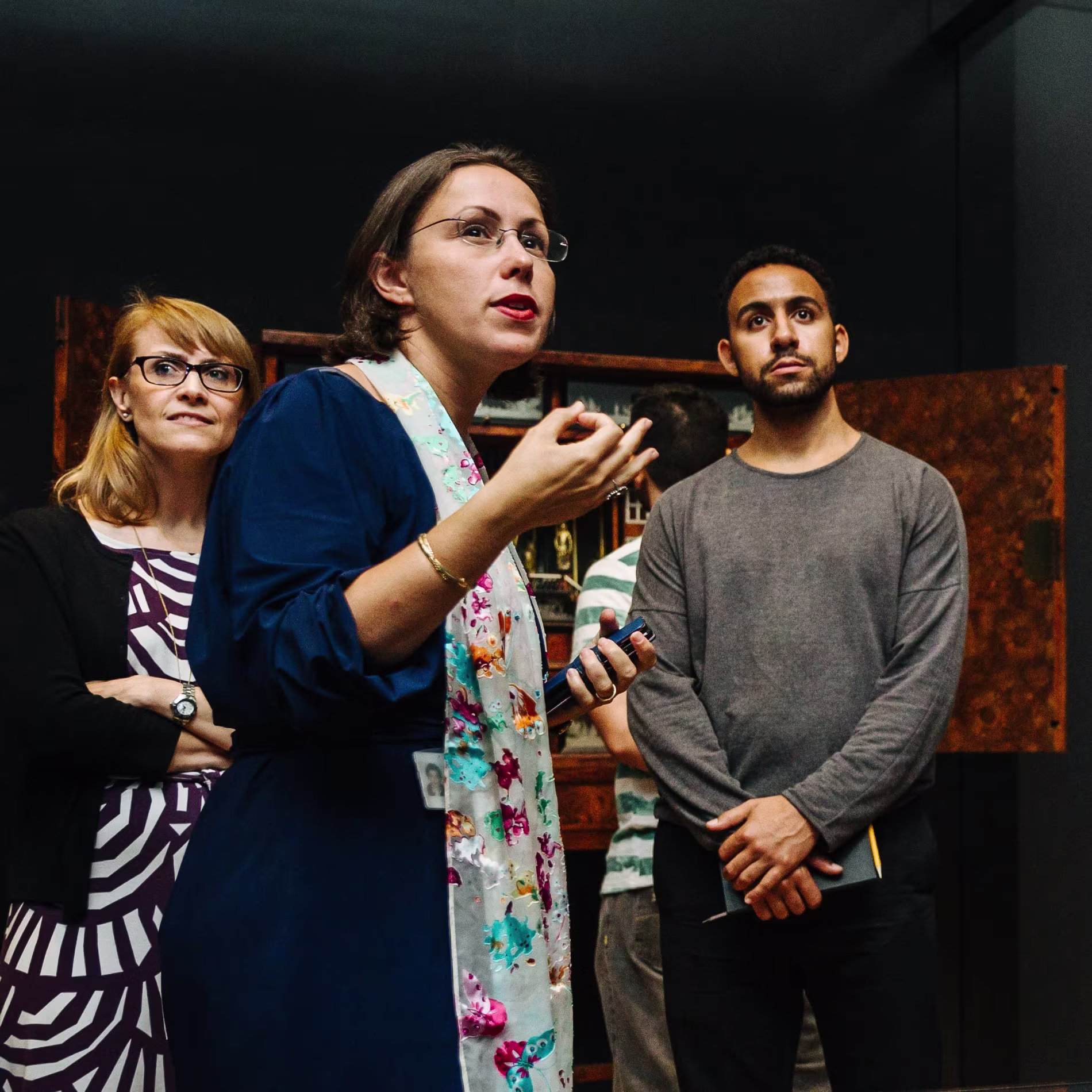 Drie mensen in gesprek op de werkplek, waarvan een vrouw met schort centraal staat te praten terwijl twee collega's luisteren.