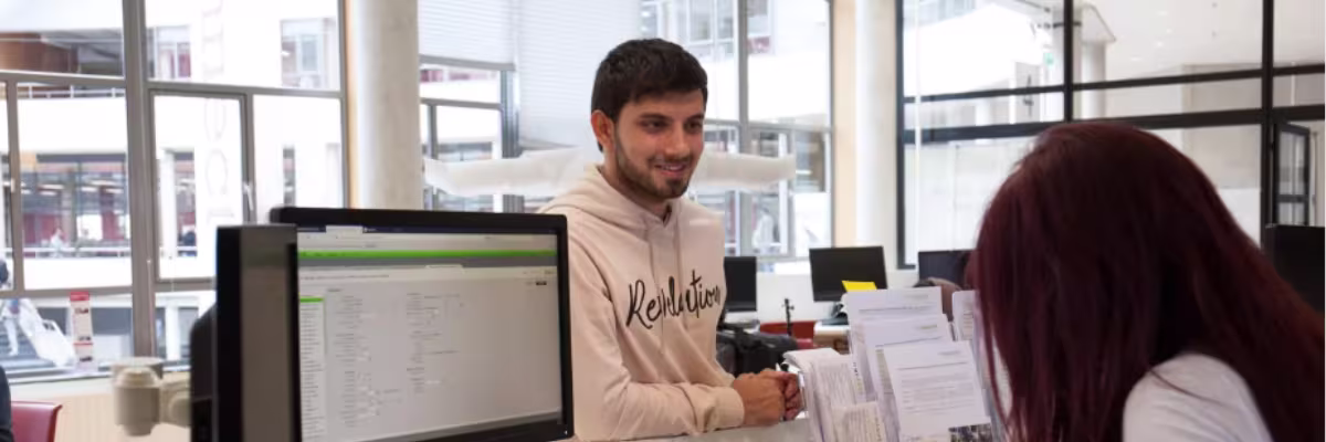 Twee medewerkers werken samen aan computers in een modern kantoor met grote ramen bij De Haagse Hogeschool.