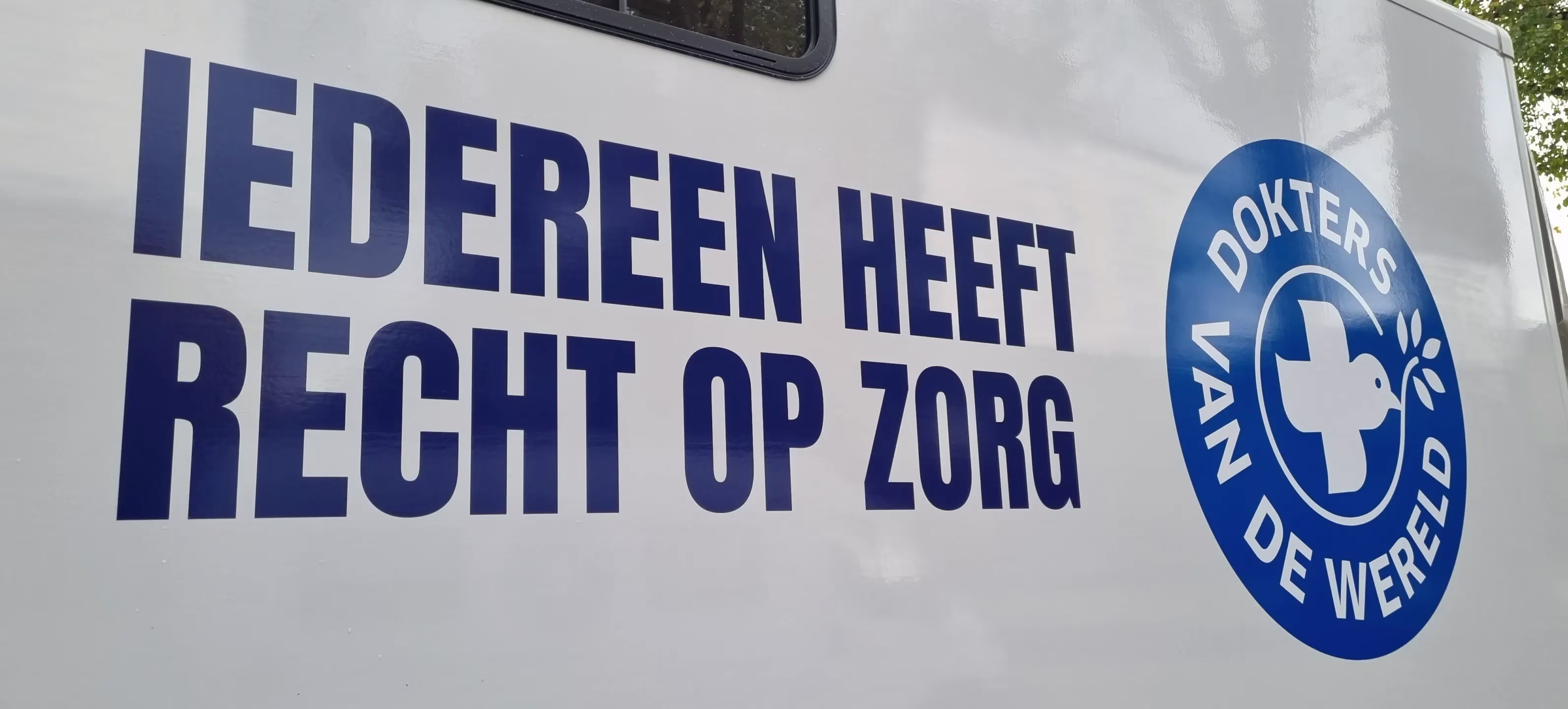 Zijkant van een witte bus met de tekst "IEDEREEN HEEFT RECHT OP ZORG" en het logo van Dokters van de Wereld.