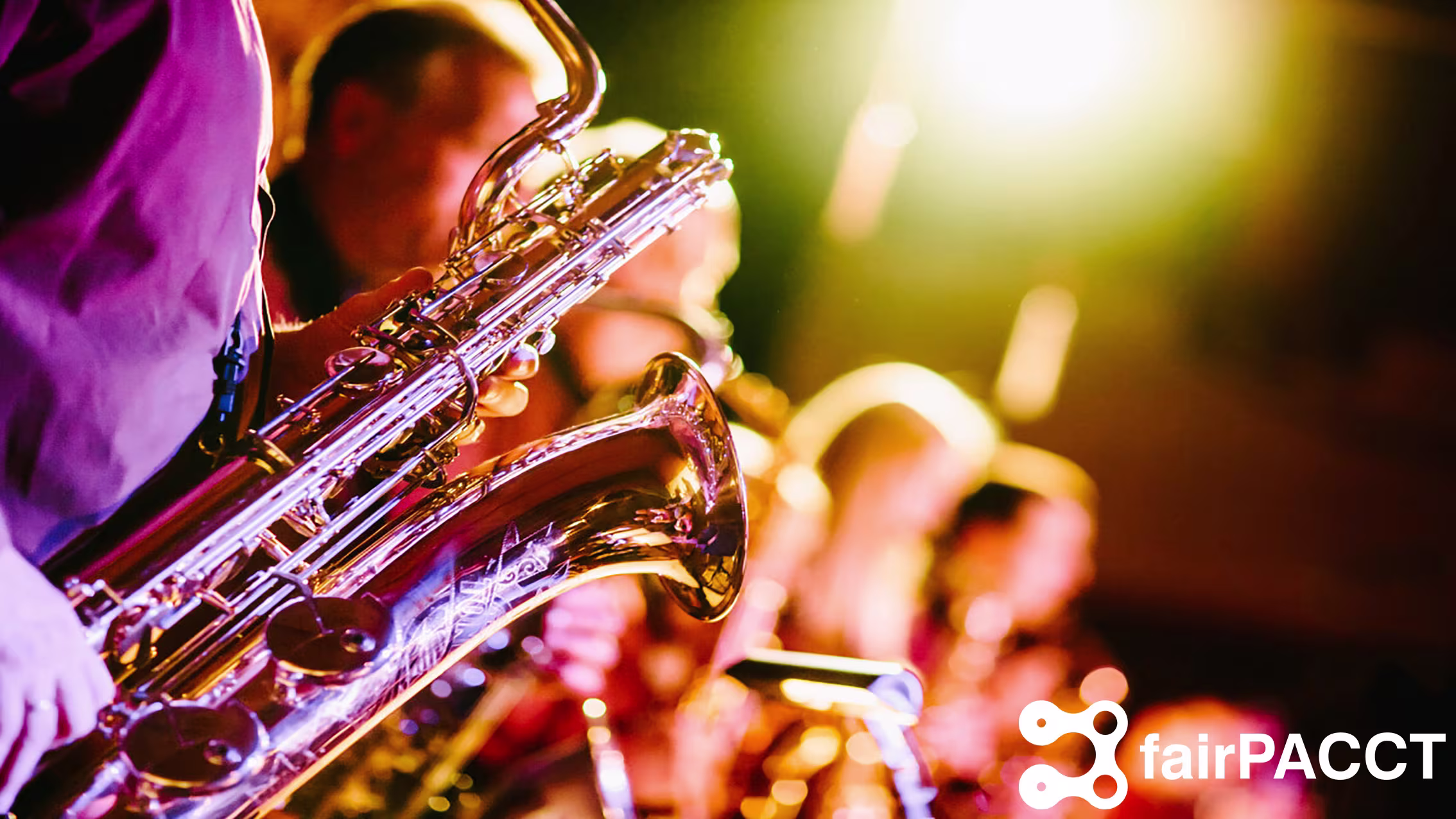 Een muzikant speelt saxofoon op het podium met warme verlichting en andere bandleden op de achtergrond.