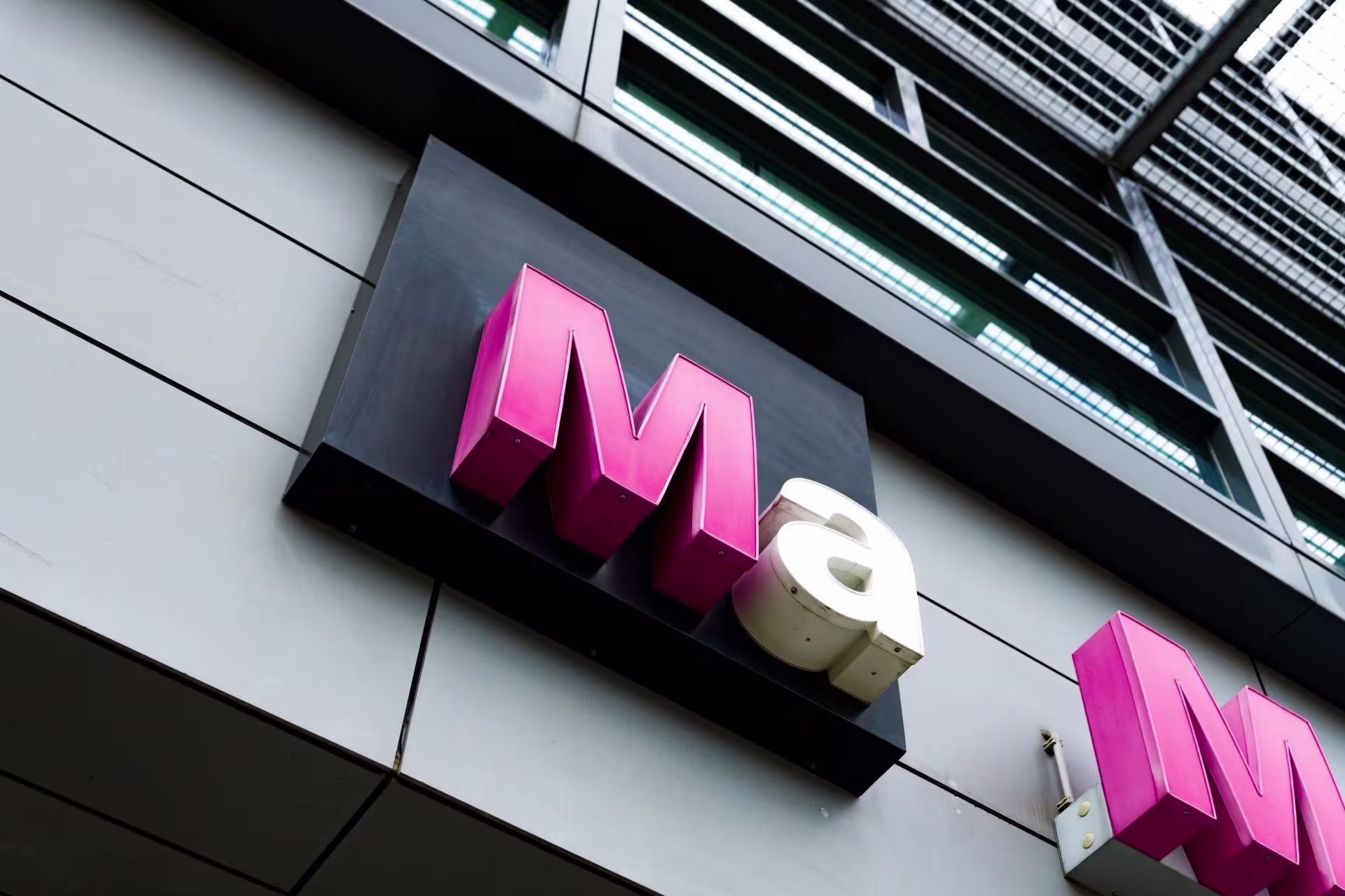 Roze logo van Mediacollege Amsterdam (Ma) op de gevel van een modern gebouw met grote ramen.