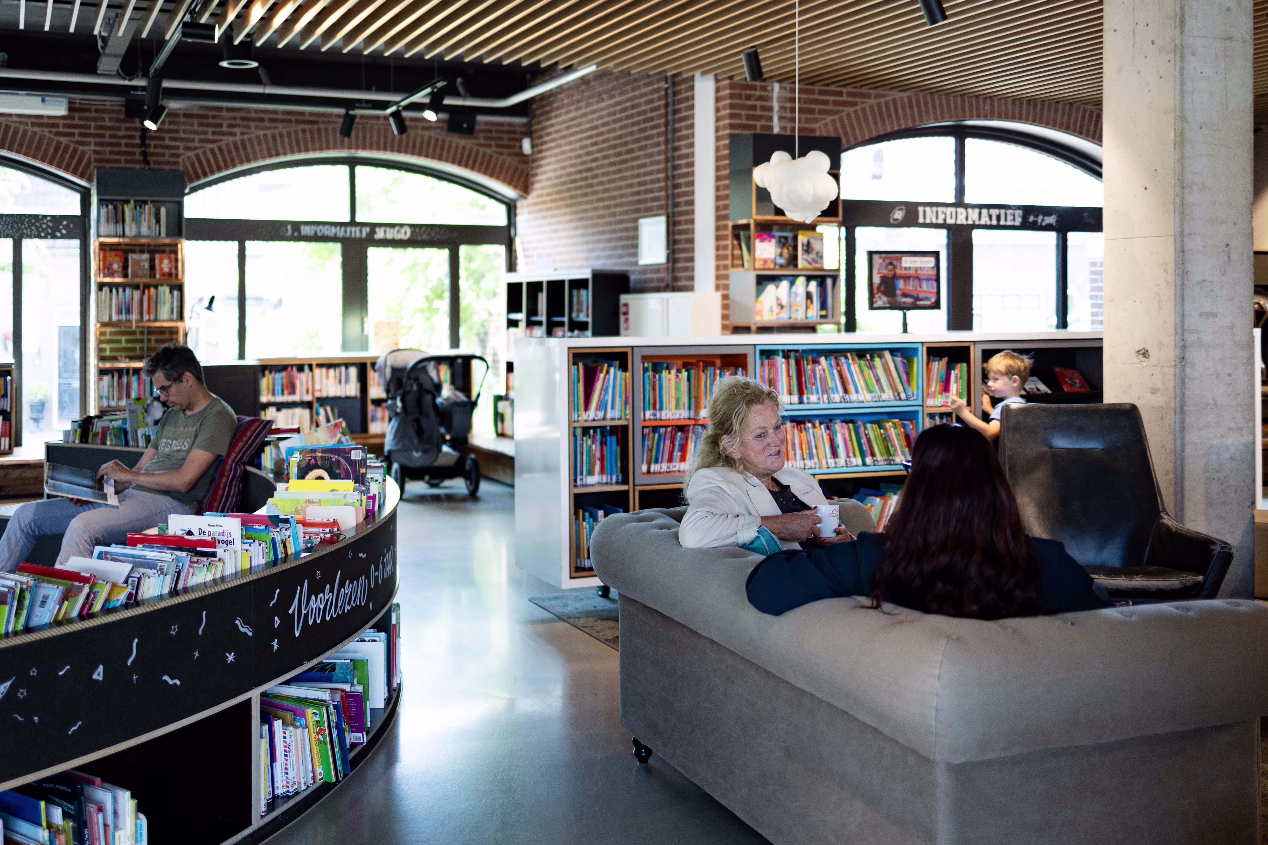 Moderne bibliotheek met mensen die lezen en werken tussen boekenkasten, met comfortabele zitplekken en grote ramen.