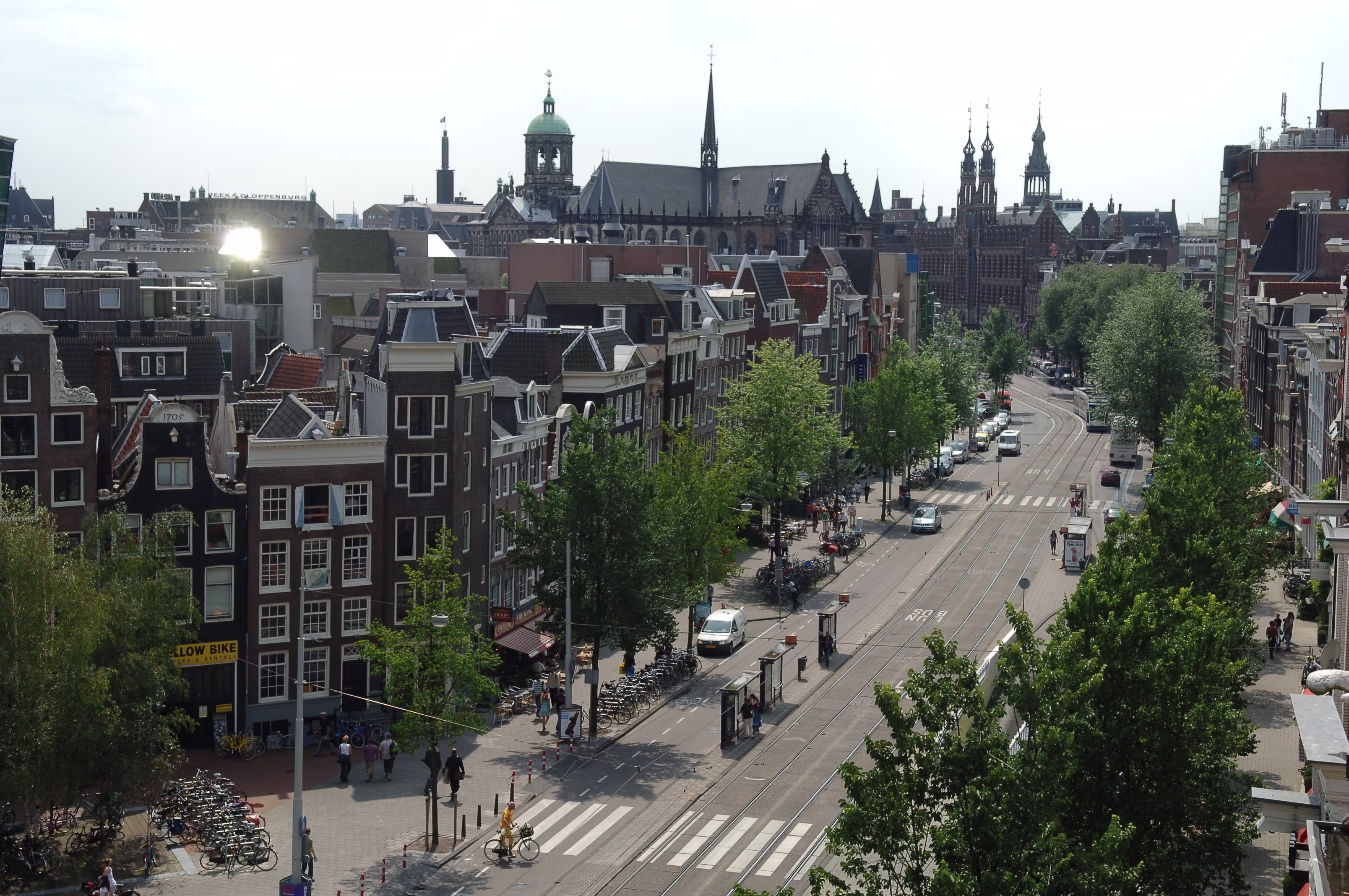 Uitzicht over Amsterdam met historische grachtenhuizen, tramsporen en kerktorens op de achtergrond.