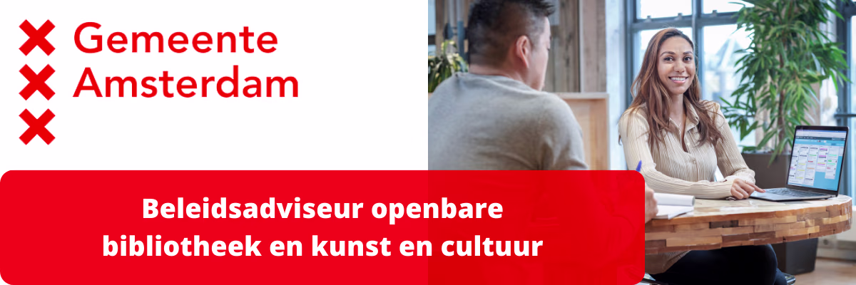 Een vrouw en man in gesprek aan een tafel met laptop in een modern kantoor met planten en grote ramen.