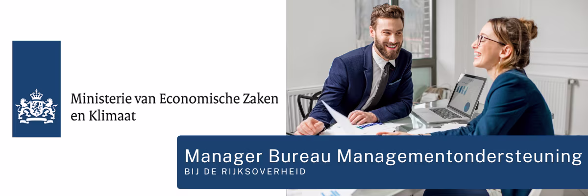 Twee professionals in pak zitten lachend aan een bureau met laptop en documenten in een modern kantoor van het ministerie.